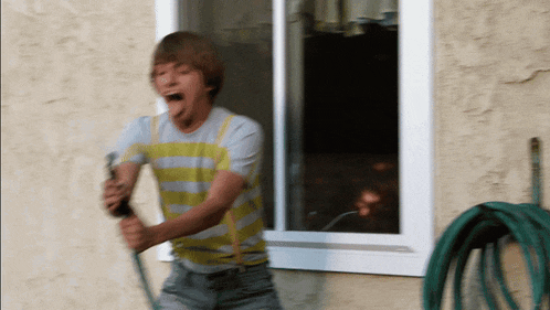 a boy is playing with a hose outside of a window