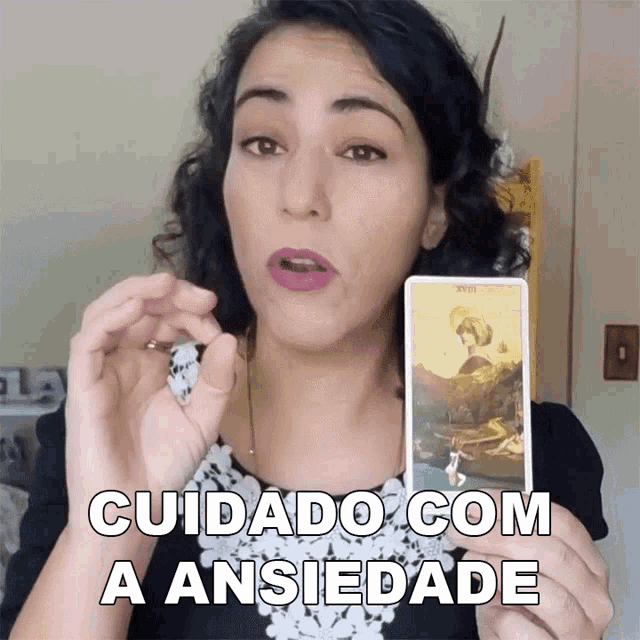 a woman holding a tarot card with the words " cuidado com a ansiedade " on the bottom
