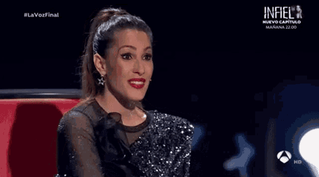 a woman in a black and silver dress is sitting in a red chair on a stage .