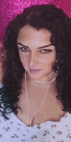 a woman with curly hair is wearing headphones and a necklace and looking at the camera .