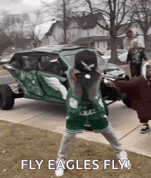 a man in a green eagles jersey is holding a baseball cap in front of a green vehicle .