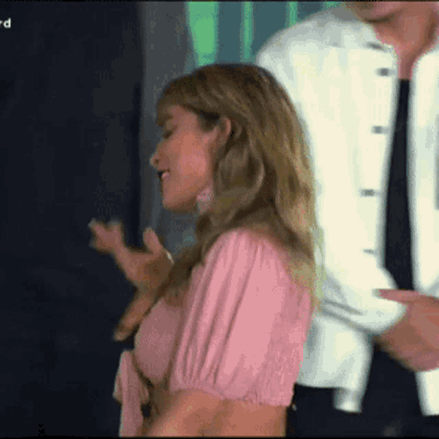 a woman in a pink top is dancing with a man in a white jacket behind her