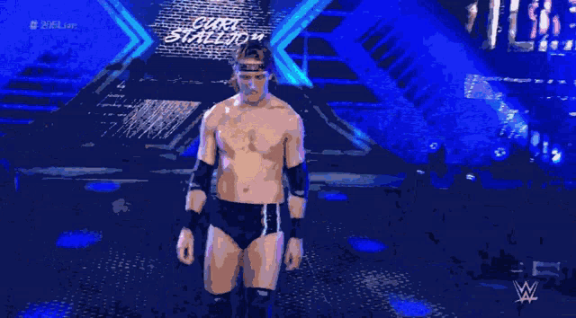 a shirtless wrestler stands in front of a blue background with the letters wwe on it