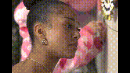 a woman is looking at herself in a mirror while wearing a bun and earrings .