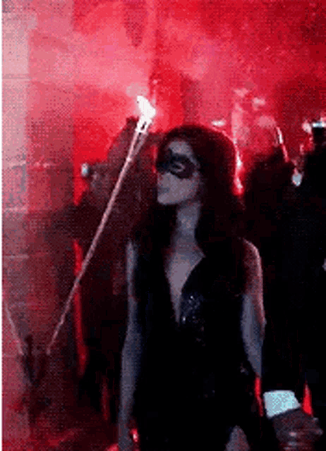 a woman wearing a mask and holding a torch in a dark room .