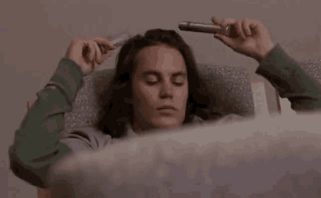 a man with long hair is laying in a chair holding a pipe to his head .