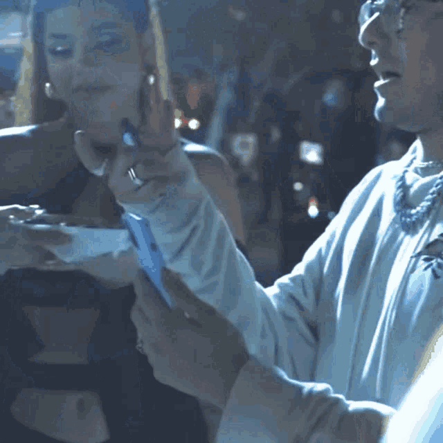 a man in a white shirt is holding a cell phone next to a woman