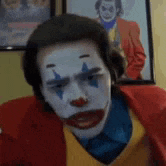 a man in a clown costume is sitting in front of a picture of the joker .