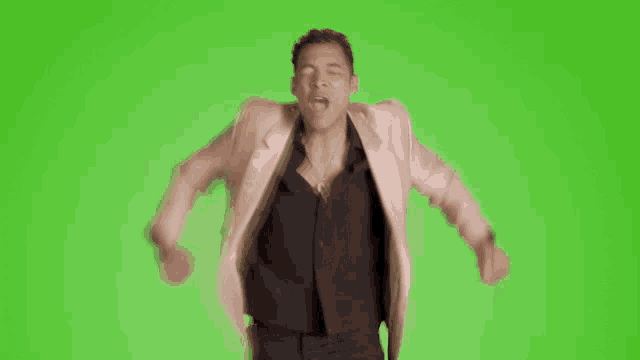 a man in a pink jacket and black shirt is screaming with his arms outstretched on a green screen