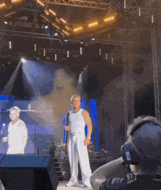 a man holding a microphone stands on a stage in front of a crowd