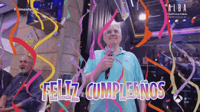 a man in a blue shirt is holding a microphone in front of confetti and the words feliz cumpleanos