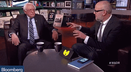 two men are sitting at a table with bloomberg in the corner