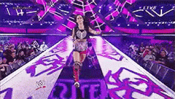 a woman is walking down a purple ramp in front of a crowd at a wrestling match .