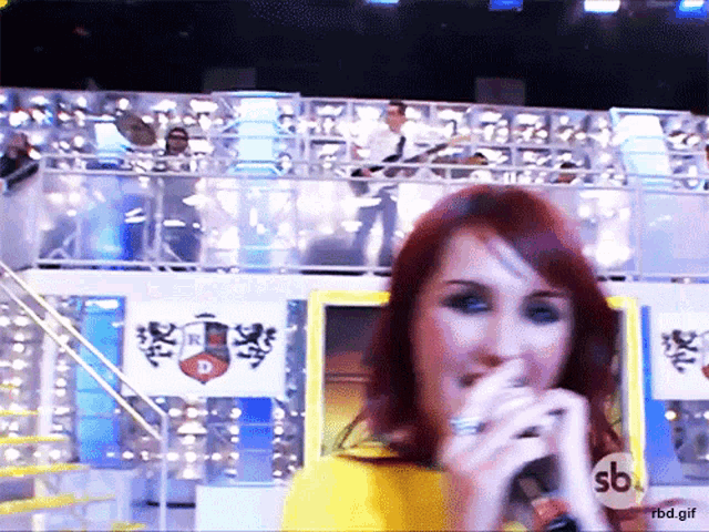 a woman singing into a microphone with a sb logo on the bottom right