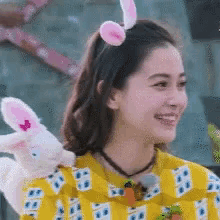 a woman wearing bunny ears and a yellow shirt is holding a stuffed rabbit .