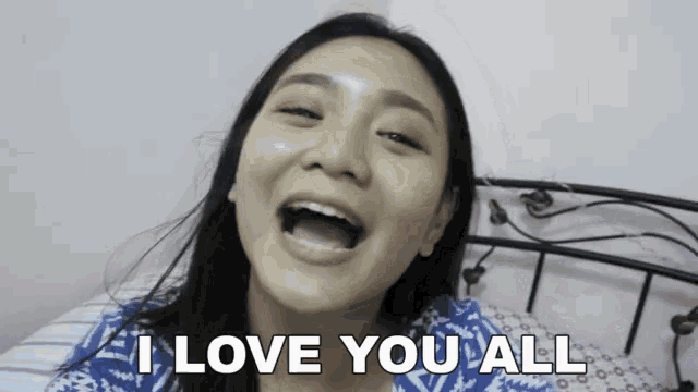 a woman is sitting on a bed making a funny face and saying `` i love you all '' .
