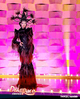 a drag queen is standing on a stage in front of a wall that says drag space
