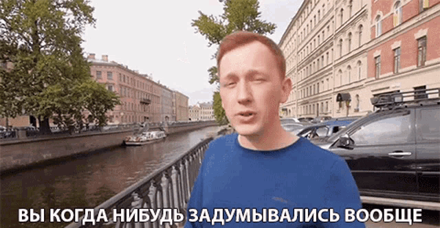 a man in a blue shirt is standing in front of a river with a caption in russian