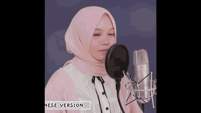a woman in a pink hijab singing into a microphone with the word nese version below her