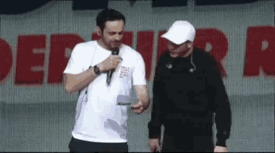 two men are standing next to each other on a stage with a microphone in their hands .
