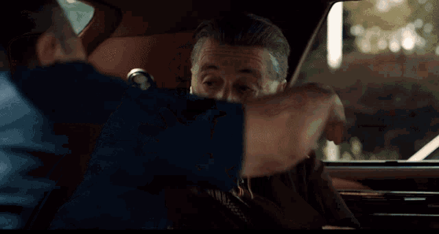 a man in a blue shirt is hugging another man in a red car