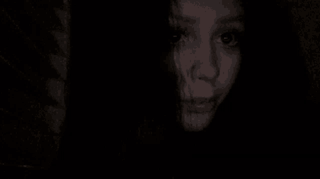 a close up of a woman 's face in the dark with a scary look on her face .