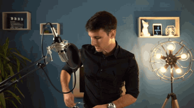 a man in a black shirt is standing in front of a microphone and a fan