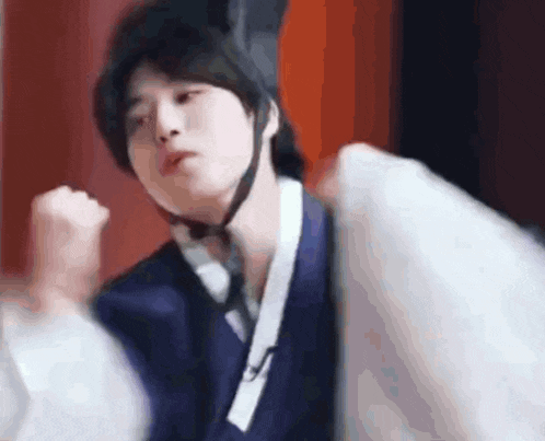 a man in a kimono is holding a pillow in his hand and making a funny face .