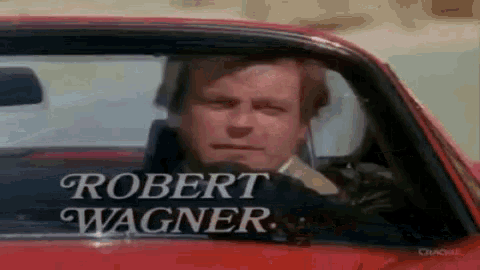 a man is sitting in a red car with the name robert wagner written on the window .