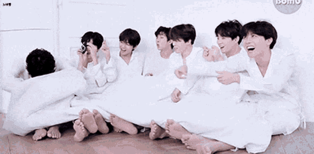 a group of young men are laying on the floor covered in white sheets