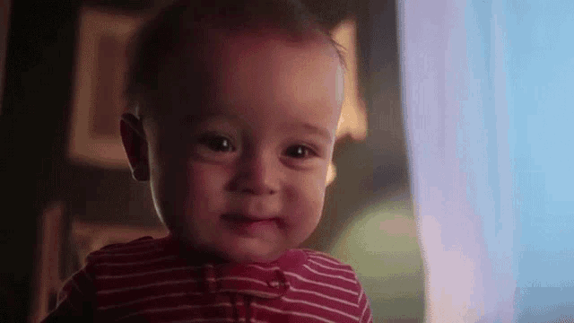a baby in a red and white striped shirt is smiling for the camera .