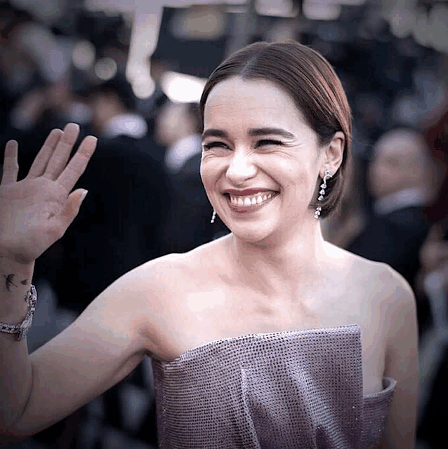 a woman in a purple dress smiles and waves