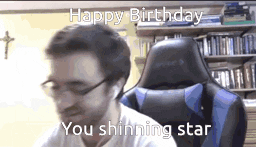 a man wearing glasses is sitting in a chair with the words `` happy birthday you shinning star '' written on the screen .