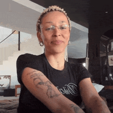 a woman wearing glasses and a black shirt has a tattoo on her arm that says ' i 'm a girl '