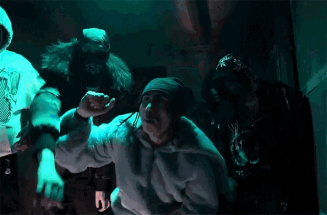 a group of people are standing in a dark room and one of them is wearing a blue fur coat