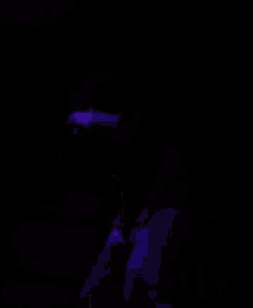 a man in a black shirt is singing into a microphone in a dark room with purple lights