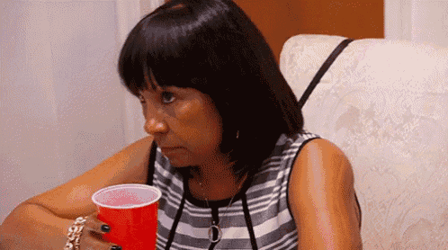 a woman is sitting on a couch holding a red cup and making a funny face .