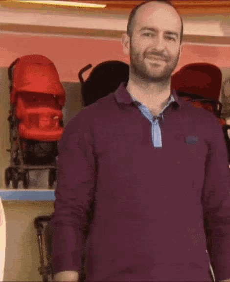a man in a purple shirt is standing in front of a display of stroller seats