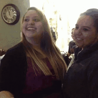 two women are smiling in front of a wall clock that shows the time as 4:20
