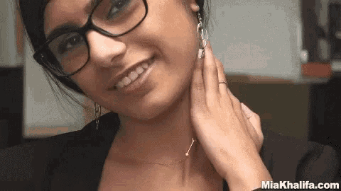 a woman wearing glasses and a necklace is smiling while touching her neck .