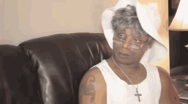 a woman is sitting on a couch wearing a white hat and glasses .