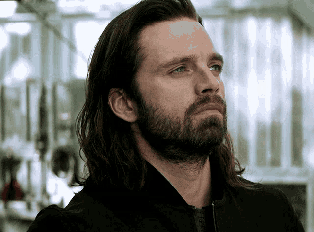 a man with long hair and a beard looks to his left