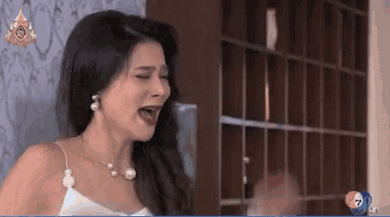 a woman in a white dress and pearl necklace is crying and screaming .