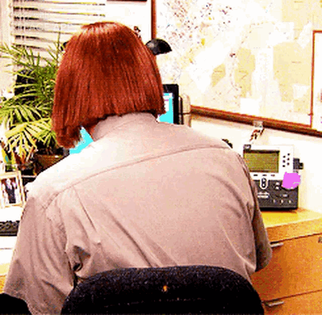 a woman with red hair is sitting at a desk in front of a cisco phone
