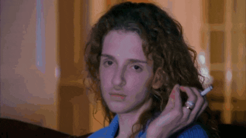 a woman with curly hair is holding a cigarette in her hand