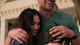 a man and a woman are hugging a child while a man scratches his head .