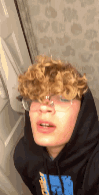 a young man with curly hair wearing glasses and a black hoodie with a blue logo on it
