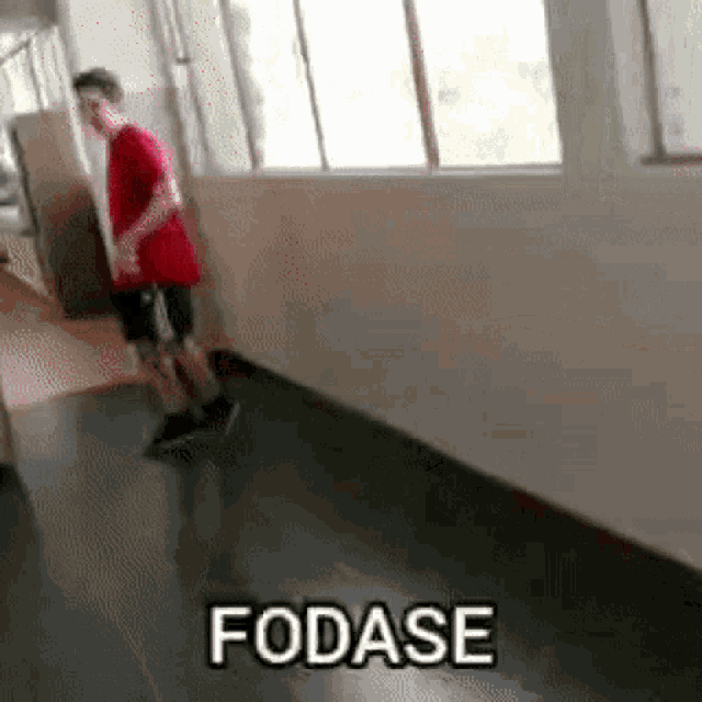 a man in a red shirt is walking down a hallway and the word fodase is written on the floor .