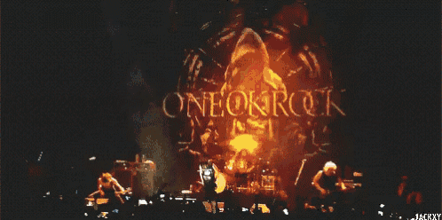 a group of people are standing on a stage watching a band perform .