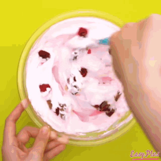 a person is stirring a bowl of pink and white ice cream with raspberries and chocolate chips .